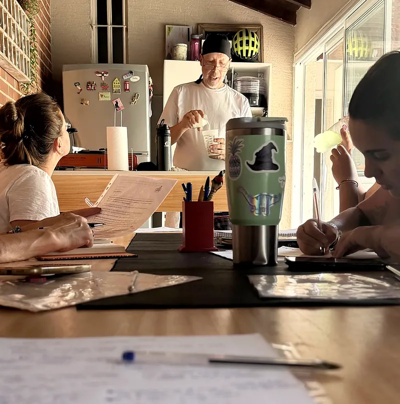 Carlos explicando frente a la mesa mientras dos alumnas toman notas